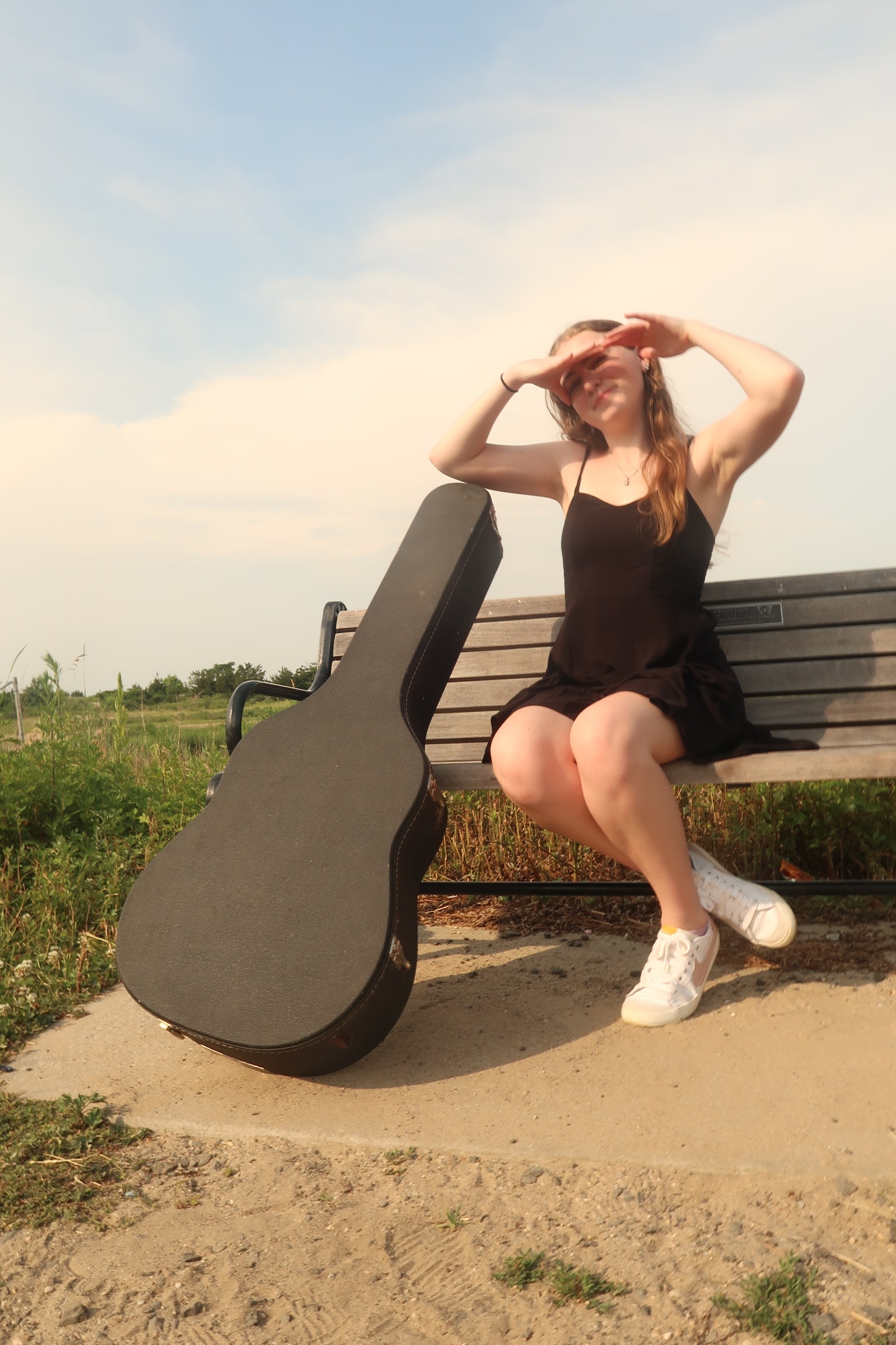 Sydneypacoustic sitting on a bench with her hands shielding her eyes from the sun